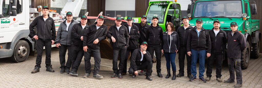 Gruppenfoto aller Mitarbeiter vor dem Firmengebäude. Die Firmenwagen im Hintergrund.
