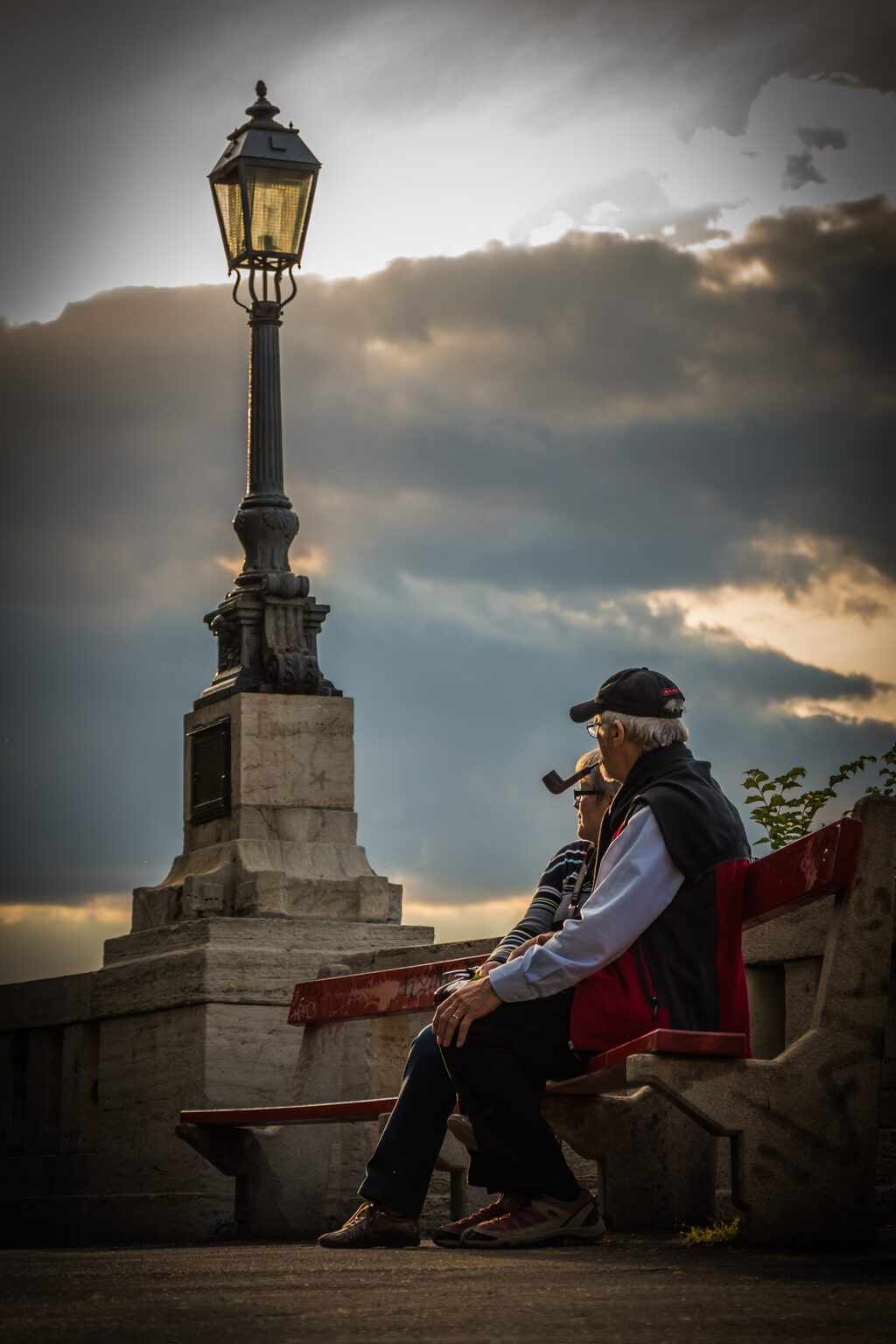 Elder couple sitting on bench by bridge with lamp