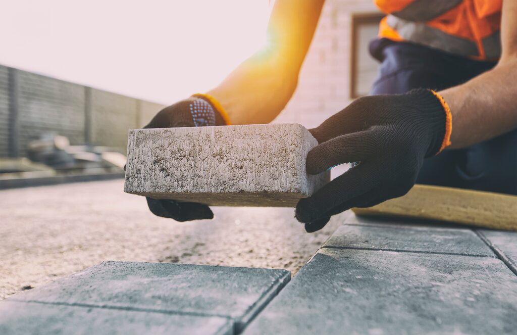 Nahaufnahme: Ein Pflasterstein wird während der Verlegung in ein Sandbett gesetzt.