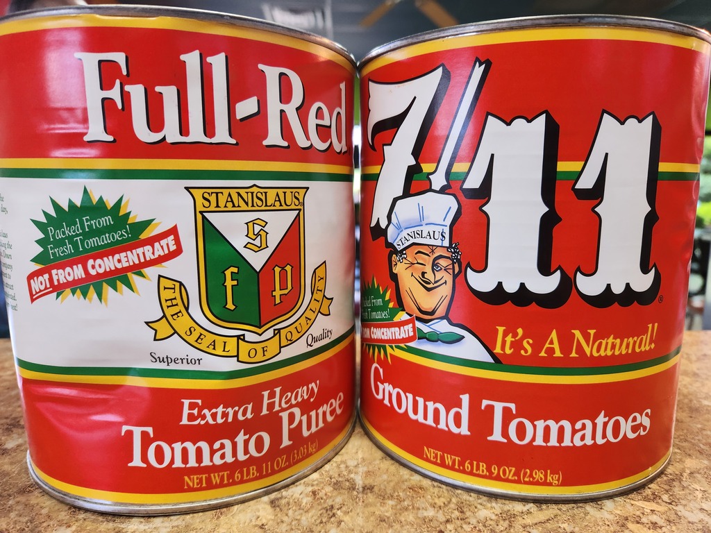 Two upcycled tomato cans that hold red pepper flakes, cheese, salt, and black pepper.