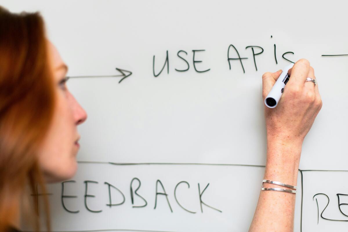 A woman writing “Use APIs” on a whiteboard during software planning