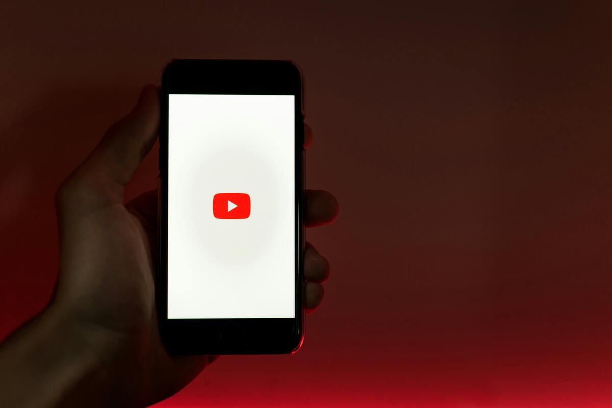 A hand holding a smartphone showing the YouTube app against a red background