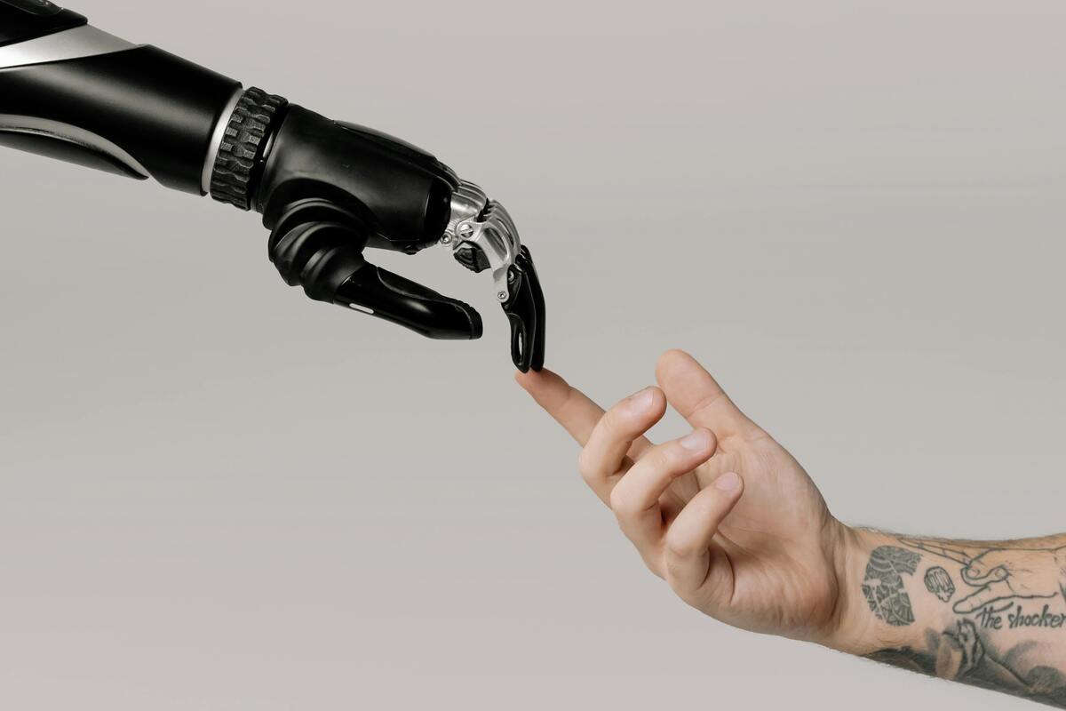 A tattooed human hand reaching toward a robotic hand on a white background