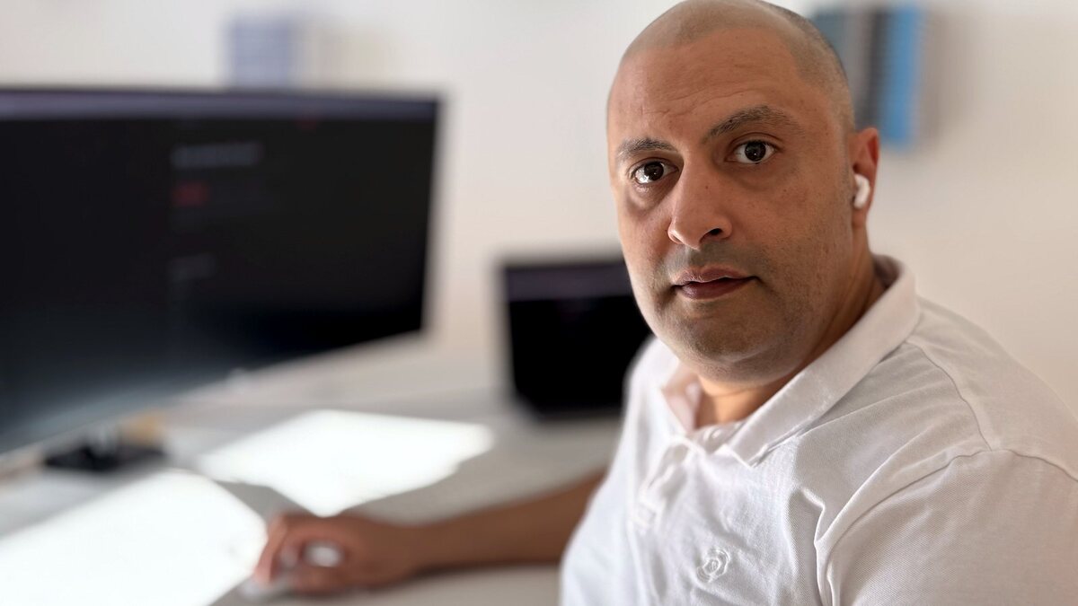 Daniel Hmaidan am Schreibtisch, im Hintergrund der Monitor mit einer Website