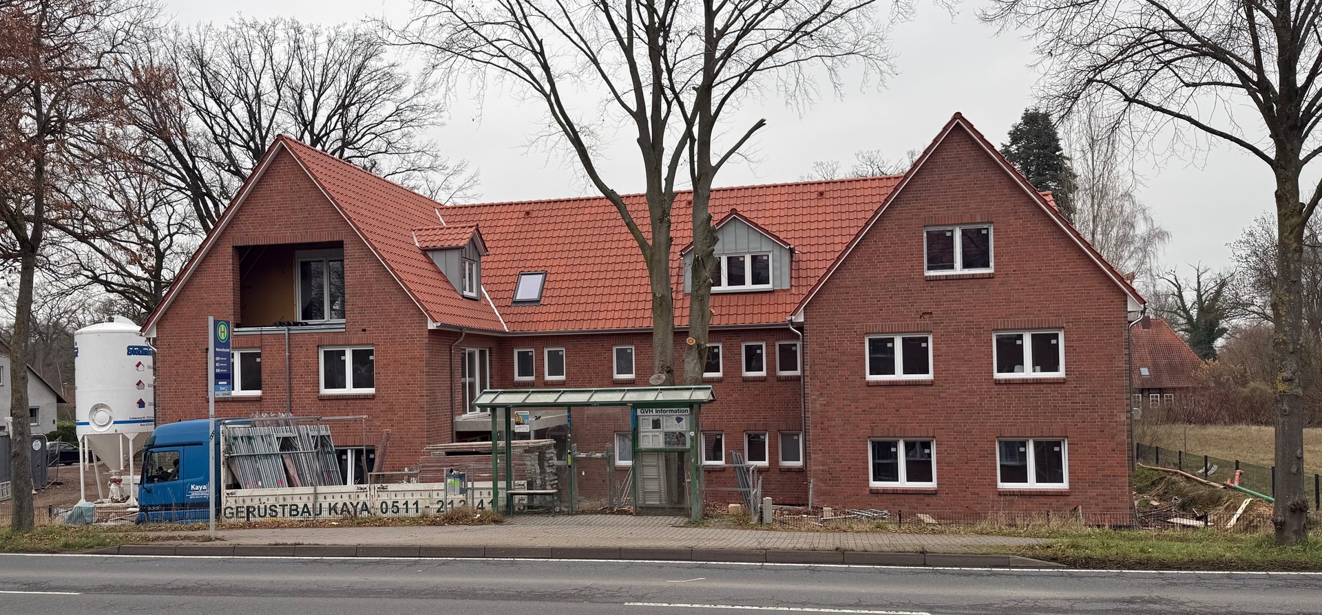 Mehrfamilienhaus im Bau mit Gerüst und Bäumen davor