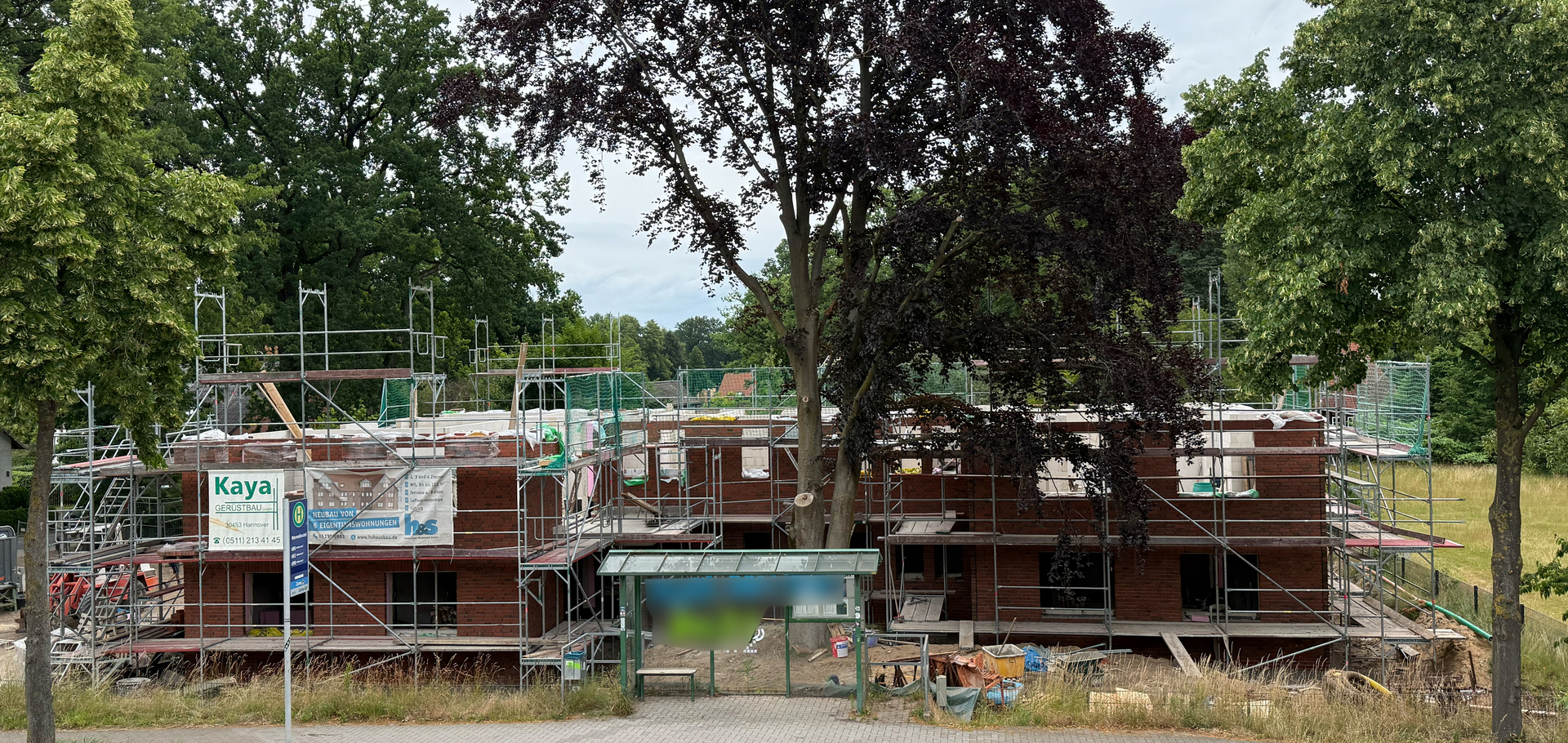 Mehrfamilienhaus im Bau mit Gerüst und Bäumen davor