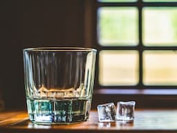Leeres Glas neben zwei schmilzenden EIswürfeln- Hypnose hilft bei Alkoholsucht