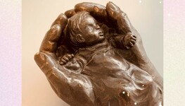 Ein Baby das in zwei Händen liegt als Figur dargestellt