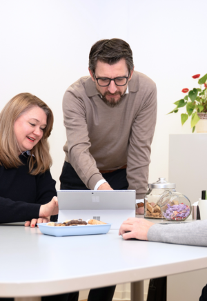 Personen sitzen an einem Tisch mit einem geöffneten Buch und Notizblöcken, eine Person hält einen grünen Stift.