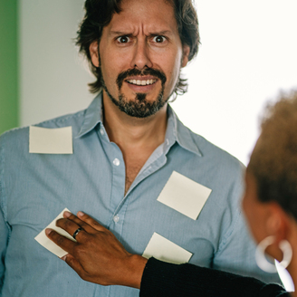 Werbeagentur für Startups & Gründer*innen: Daniel Kaesmacher guckt verdutzt während Jessica ihm diverse Post-Its auf sein Hemd klebt.