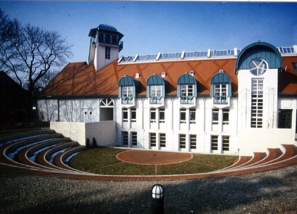 Modernes Gebäude mit roten Dächern, großen Fenstern und Freilichtbühne