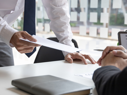 Behördliches Gespräch – Person übergibt ein Schriftstück an eine andere Person am Schreibtisch