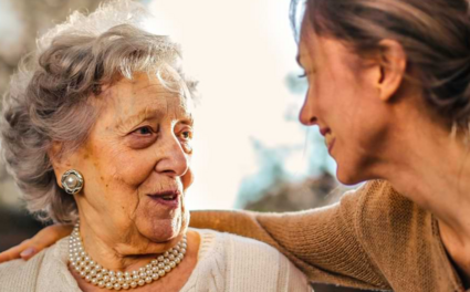 Ältere Dame und Betreuerin lächeln sich an