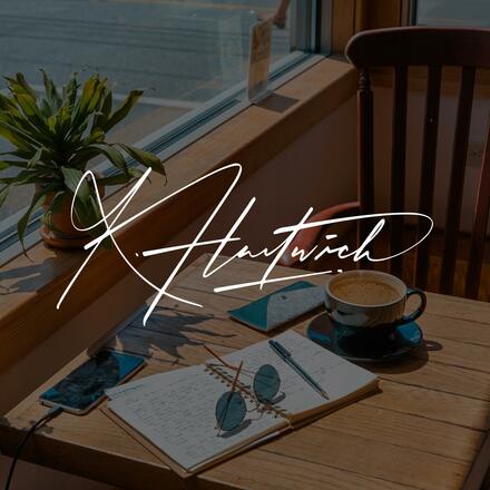  Notizbuch, Sonnenbrille und Kaffeetasse auf einem Holztisch am Fenster – darüber die Signatur „K. Hartwich“