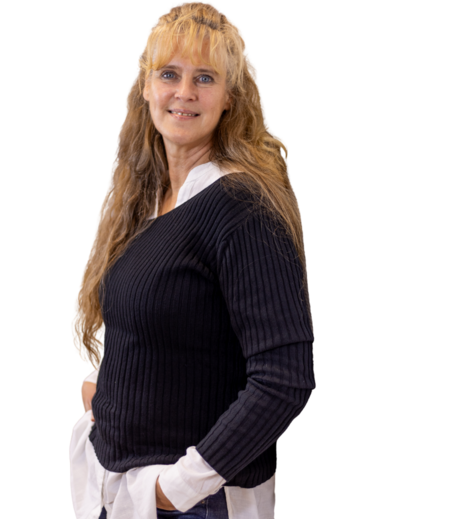 Frau mit langen, gewellten blonden Haaren trägt schwarzen Pullover über weißem Hemd und blaue Jeans, Hände in den Taschen.