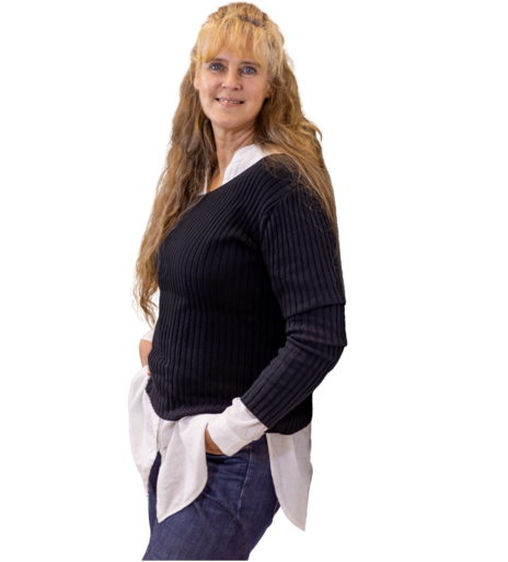 Frau mit langen, gewellten blonden Haaren trägt schwarzen Pullover über weißem Hemd und blaue Jeans, Hände in den Taschen.