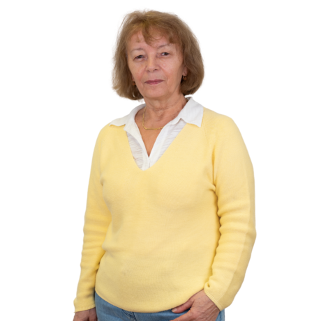 Frau mit kurzen blonden Haaren in hellviolettem Blazer, lila T-Shirt und blauen Jeans steht mit verschränkten Händen.