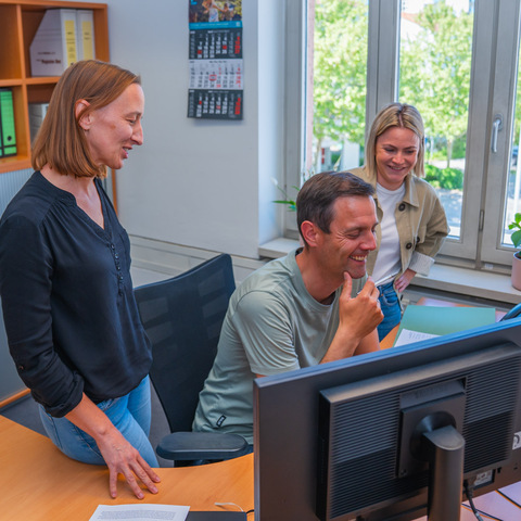 Team am Schreibtisch – Drei Mitarbeitende besprechen sich gemeinsam an einem Computer