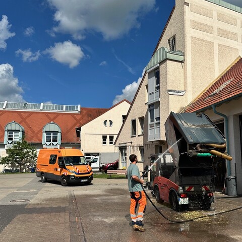 Mitarbeiter in Warnkleidung reinigt im Hof ein Fahrzeug mit einem Hochdruckreiniger