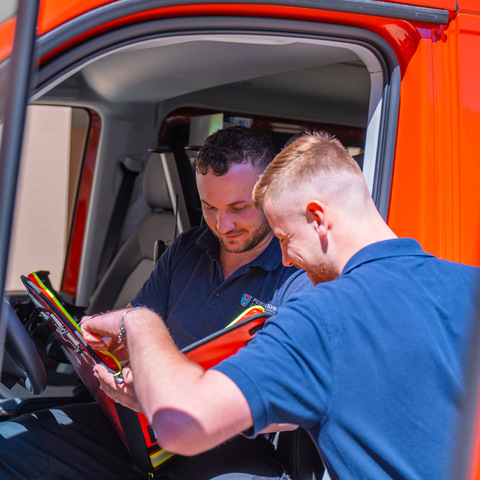 Einsatzbesprechung – Zwei Feuerwehrmänner mit Unterlagen im Fahrzeug