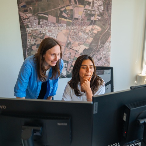 Gemeinsamer Blick auf Bildschirm – Zwei Mitarbeiterinnen betrachten konzentriert einen Monitor vor einer Stadtkarte