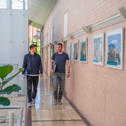 Gespräch im Flur – Zwei Mitarbeitende unterhalten sich beim Gehen durch einen hellen Flur