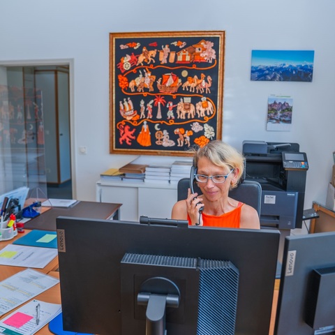 Telefonat am Empfang – Mitarbeiterin telefoniert am Arbeitsplatz mit Computer und Akten im Hintergrund