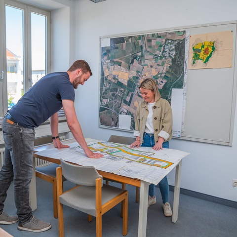 Bauplanung – Zwei Mitarbeitende betrachten gemeinsam einen großen Stadtplan auf einem Tisch