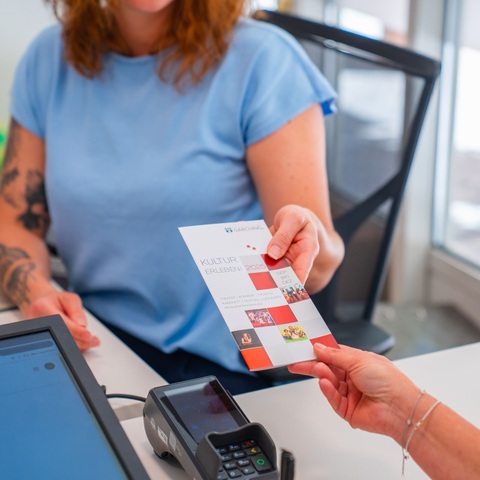 Flyerübergabe im Kulturbüro – Eine Mitarbeiterin übergibt einer Besucherin einen Kulturflyer