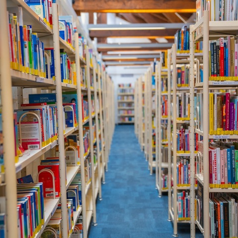 Bücherregale in der Stadtbücherei – Blick durch eine lange Regalreihe voller Bücher in der Stadtbücherei