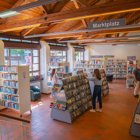 Marktplatz der Stadtbücherei – Offener Bereich der Stadtbücherei mit Regalen für Romane und CDs, Besucher stöbern in den Medien