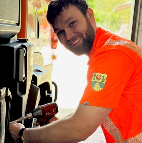 Mitarbeiter in Warnkleidung repariert ein Fahrzeugteil mit einem Akkuschrauber