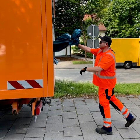 Mitarbeiter in Warnkleidung wirft einen Müllsack in ein Sammelfahrzeug