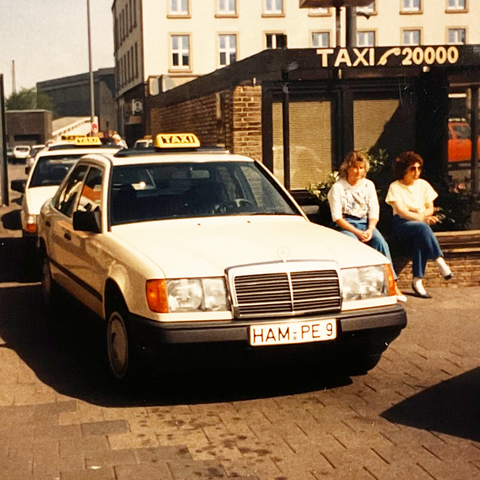 Taxengemeinschaft Hamm - Historie - Zwei Personen die neben einem Taxi auf einer Mauer sitzen