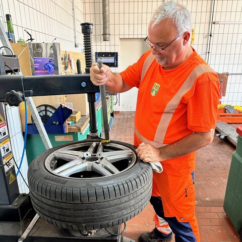 Mitarbeiter in Warnkleidung arbeitet in einer Werkstatt an einem Autoreifen