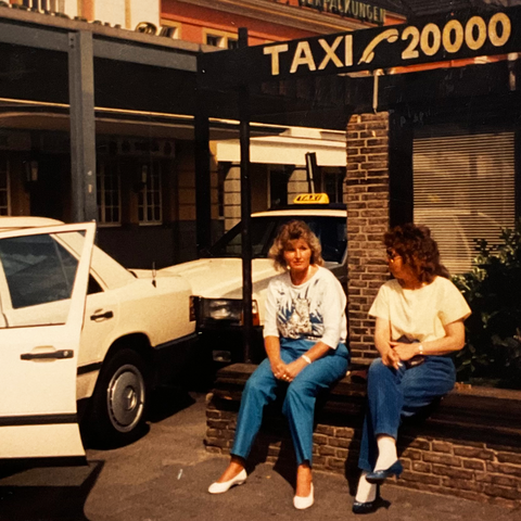 Taxengemeinschaft Hamm - Historie - Zwei Personen die neben einem Taxi auf einer Mauer sitzen