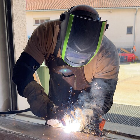 Schweißer mit Schutzmaske arbeitet an einem Metallteil, Funken fliegen