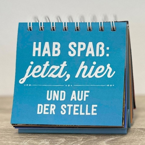 Kalenderspruch – Blauer Tischkalender mit der Aufschrift „Hab Spaß: jetzt, hier und auf der Stelle“