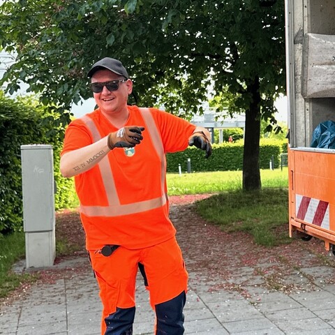 Mitarbeiter in orangefarbener Warnkleidung lächelt und gestikuliert während der Arbeit im Freien