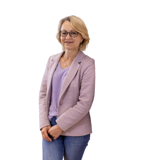 Frau mit kurzen blonden Haaren in hellviolettem Blazer, lila T-Shirt und blauen Jeans steht mit verschränkten Händen.