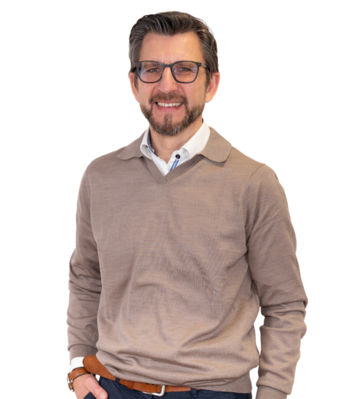 Dirk Kastner stehend im weißem Hemd mit dunklen Knöpfen, blauer Hose, braunem Gürtel und Armbanduhr.