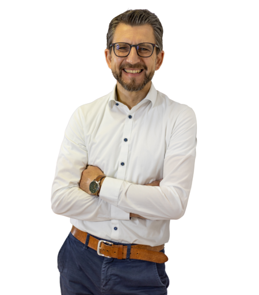 Dirk Kastner steht mit verschränkten Armen, lächelt in die Kamera, trägt ein weißes Hemd und blaue Hose.