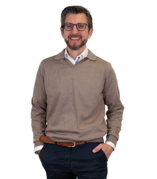 Dirk Kastner steht mit verschränkten Armen, lächelt in die Kamera, trägt ein weißes Hemd und blaue Hose.