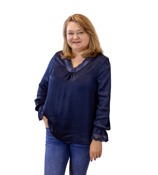 Frau mit schulterlangem, blondem Haar in dunkelblauer Bluse und Ausschnitt sowie blauen Jeans.