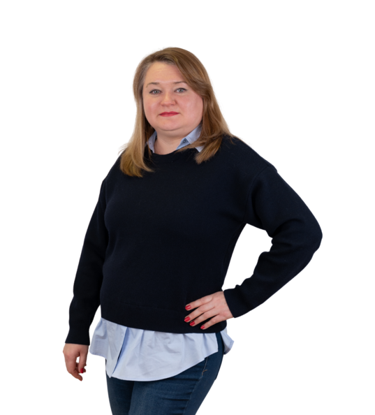 Frau mit schulterlangem, blondem Haar in dunkelblauer Bluse und Ausschnitt sowie blauen Jeans.