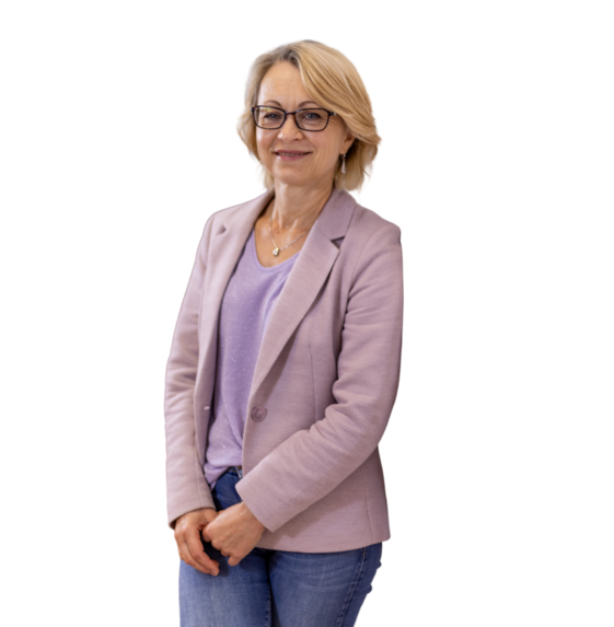 Frau mit kurzen blonden Haaren in hellviolettem Blazer, lila T-Shirt und blauen Jeans steht mit verschränkten Händen.