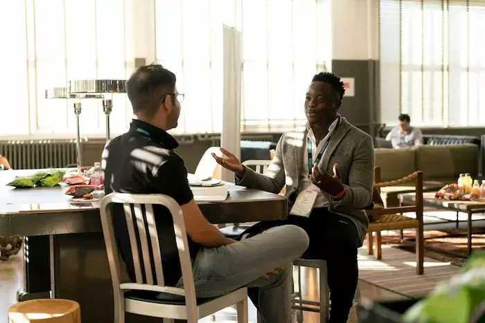 Two men having a conversation while seated in an office brightly illuminated by natural light.
