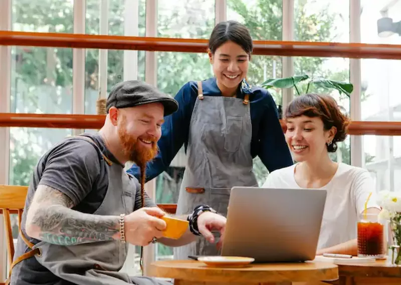 3 co-workers gathering around a laptop, smiling.