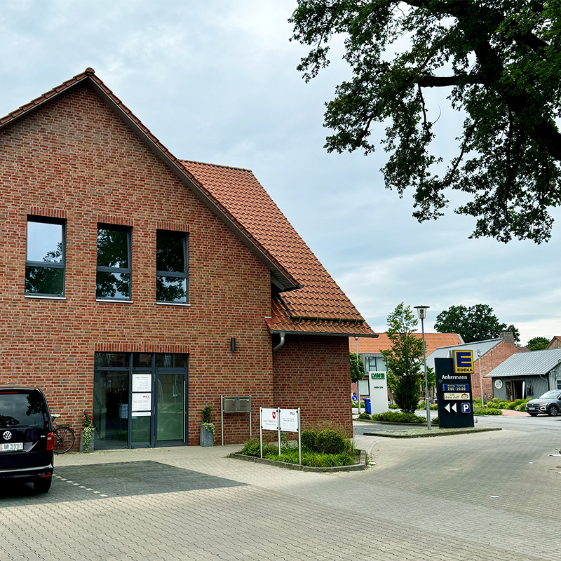 Backsteingebäude mit roten Ziegeldach, Parkplatz und Edeka-Schild im Hintergrund
