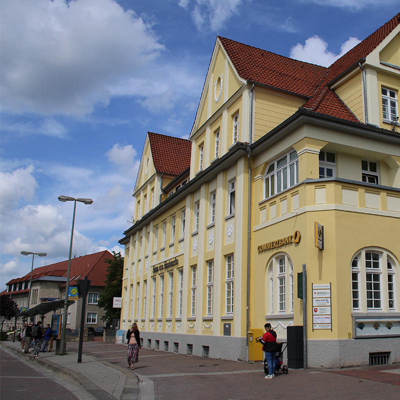 Gelbes Gebäude mit roten Ziegeldächern in Gifhorn, Commerzbank-Filiale im Erdgeschoss, Menschen auf dem Gehweg